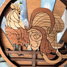 Load image into Gallery viewer, Three-layered Christmas ornament, approximately 4" in diameter, made of multiple hardwood veneers, depicting a fancy rooster sitting on a barnyard fence with sun rays in the background. Made in Virginia by @BelCreativeArts.